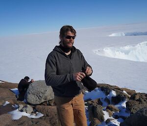 Two expeditioners at the top of a rocky hill with snow and clear blue skies in the background