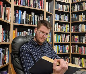 A studious Tom Herbert in the Casey library post-haircut, reading a large book and wearing glasses and a smart shirt