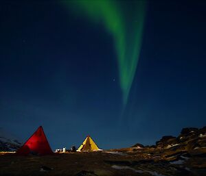 A red and a yellow tent lit from inside, against the night sky which is dominated by a green Aurora