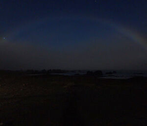 Very dark shot of the night sky with a lunar rainbow visible over the station