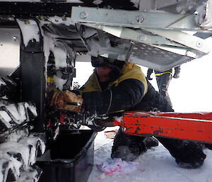 Mechanic making repairs underneath vehicle, kneeling in the ice.