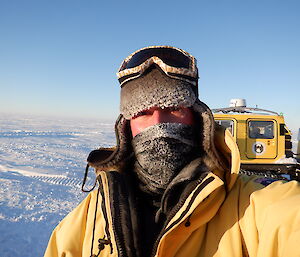 Portrait of expeditioner with cold weather gear.  Only eyes are uncovered on his face.  Ice in background.