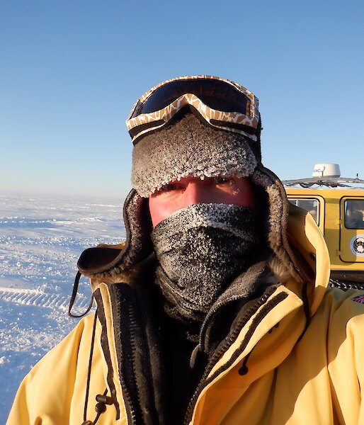 Portrait of expeditioner with cold weather gear.  Only eyes are uncovered on his face.  Ice in background.