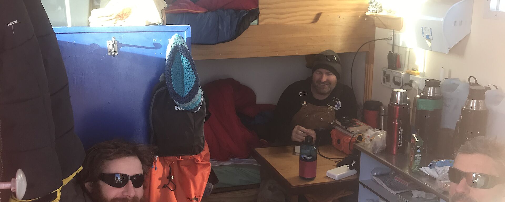 Four expeditioners inside a small hut sitting eating.  Bunk style beds in background.