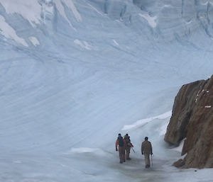 Three expeditioners take a walk on some ice with large ice formation in front of them