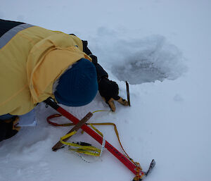 An expeditioner lying with his face close to the ice measuring snow depth