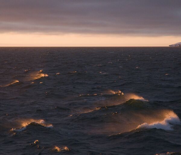 waves in the Southern ocean with an iceberg in the background