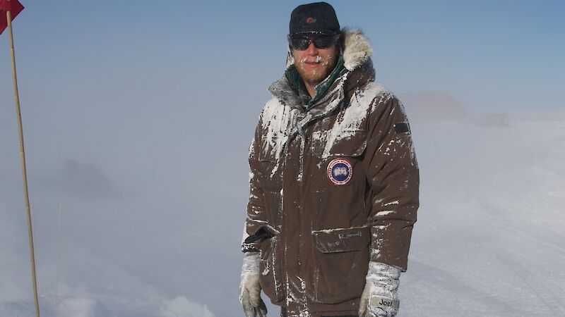 Joel Pedro stands outside in the snow with his warm clothing covered in snow.