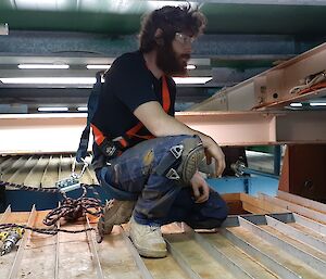 An expeditioner with protective goggles, knee pads and two capped boots on top of the large water tank