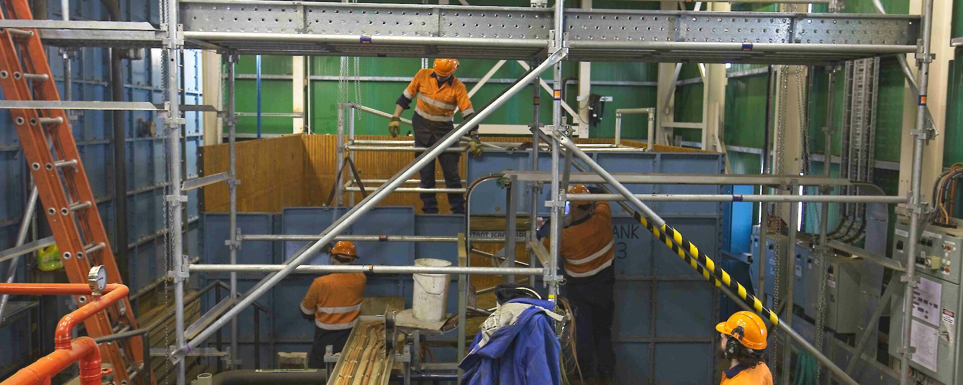 Four expeditioners work on some scaffolding wearing hard hats and hi vis gear
