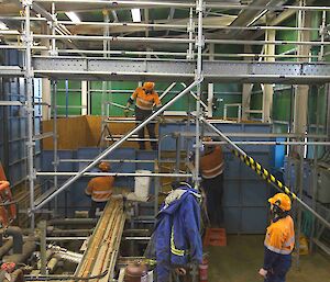 Four expeditioners work on some scaffolding wearing hard hats and hi vis gear