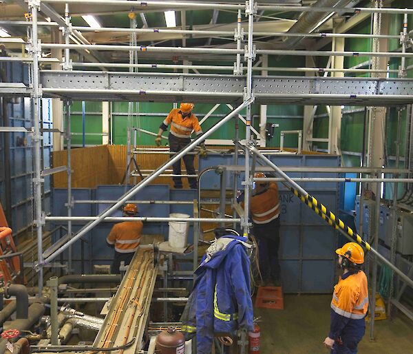 Four expeditioners work on some scaffolding wearing hard hats and hi vis gear