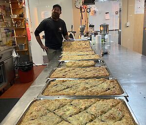 7 trays of fresh made borek on a kitchen bench with an expeditioner smiling to camera