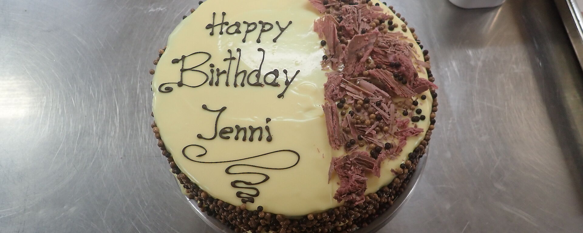 A birthday cake with Happy Birthday Jenni written on the top with chocolate shards