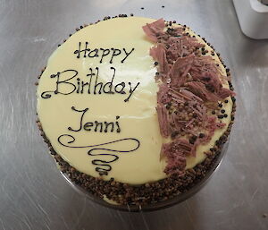 A birthday cake with Happy Birthday Jenni written on the top with chocolate shards