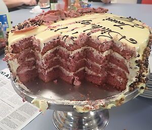 A birthday cake half eaten showing a red velvet centre with cream icing
