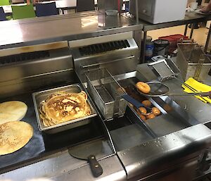 Deep fat friers and hot plates with pancakes and doughnuts being cooked