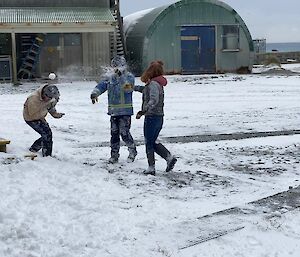 Three expeditioners in the middle of a snowball fight. A snowball thrown by Sara is exploding over George's face.