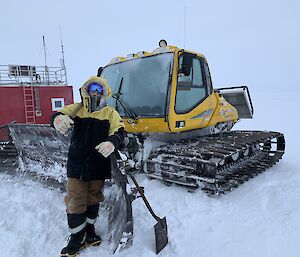 An expeditioner stands in front of a groomer leaning on a shovel