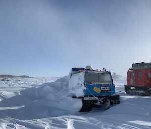 A blue Hagglund half covered with snow next to a red Hagglund