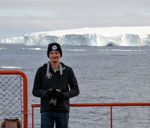 Man with camera on ship with iceberg in background