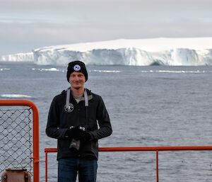 Man with camera on ship with iceberg in background