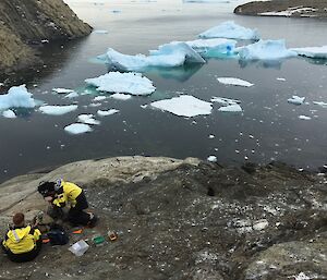 Two men on rock with camera at sea edge with blue ice