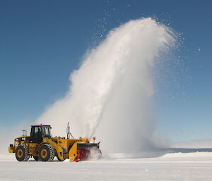 A Caterpillar tractor being used to blow snow off the ice runway.