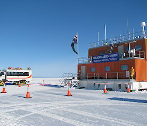 The orange building at Wilkins Aerodrome, with a snow-tracked bus alongside to collect passengers.