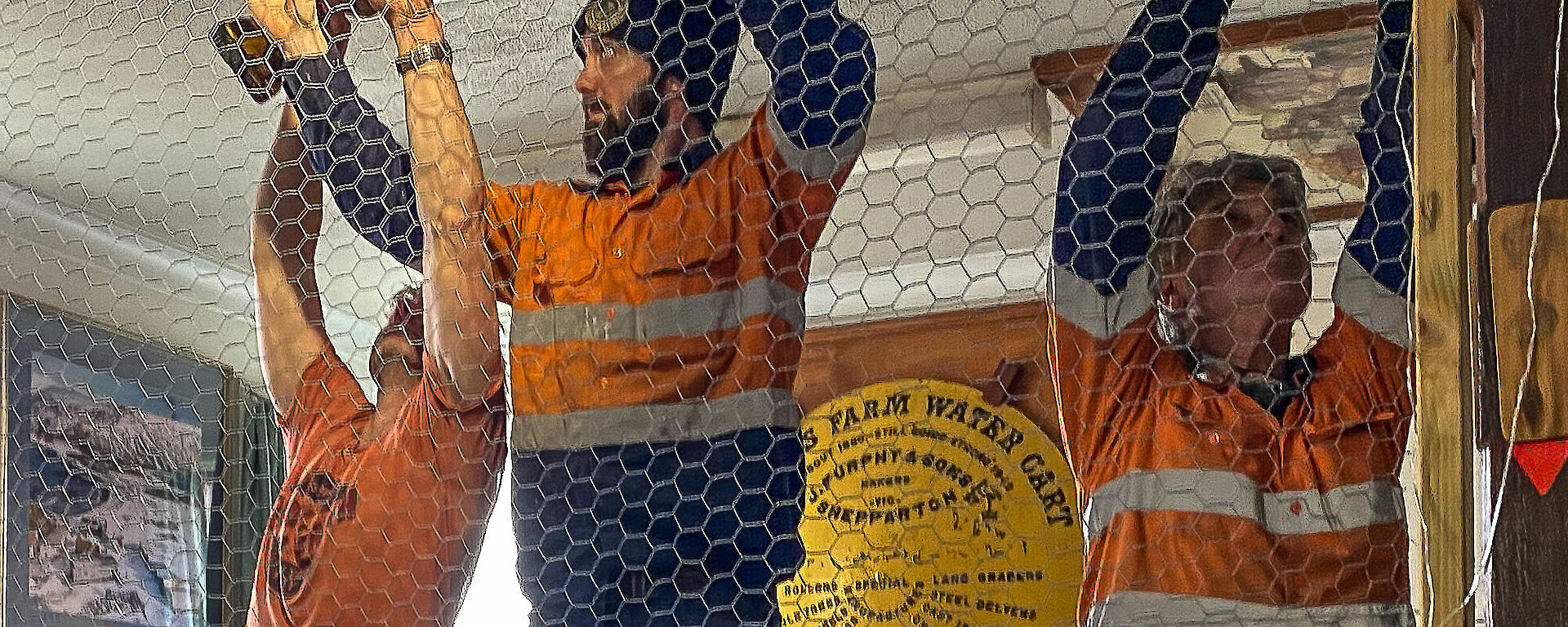 Three tradesmen putting up a chicken wire wall in the Mess