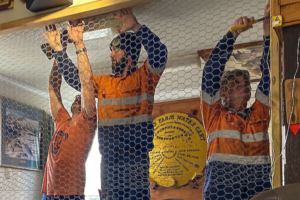 Three tradesmen putting up a chicken wire wall in the Mess