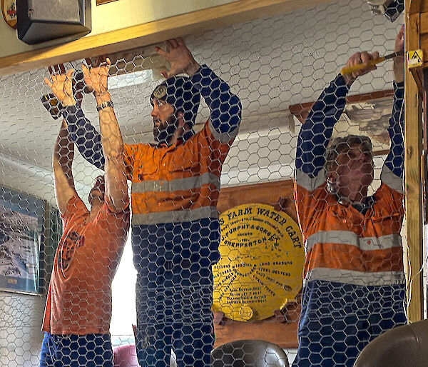 Three tradesmen putting up a chicken wire wall in the Mess