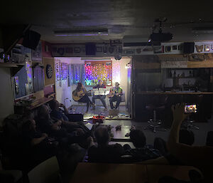 Three people playing acoustic guitar in front of a seated audience in the Mess