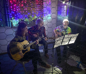 Three people sitting down playing acoustic guitars