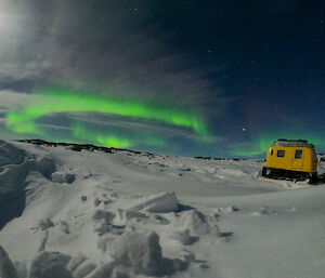 An aurora above the Browning Peninsula with the yellow Hägglunds in the foreground