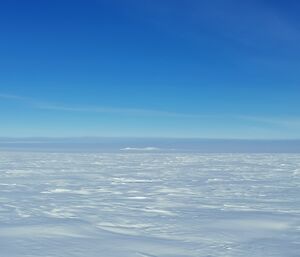 A snow covered landscape with snow covered nunataks in the distance