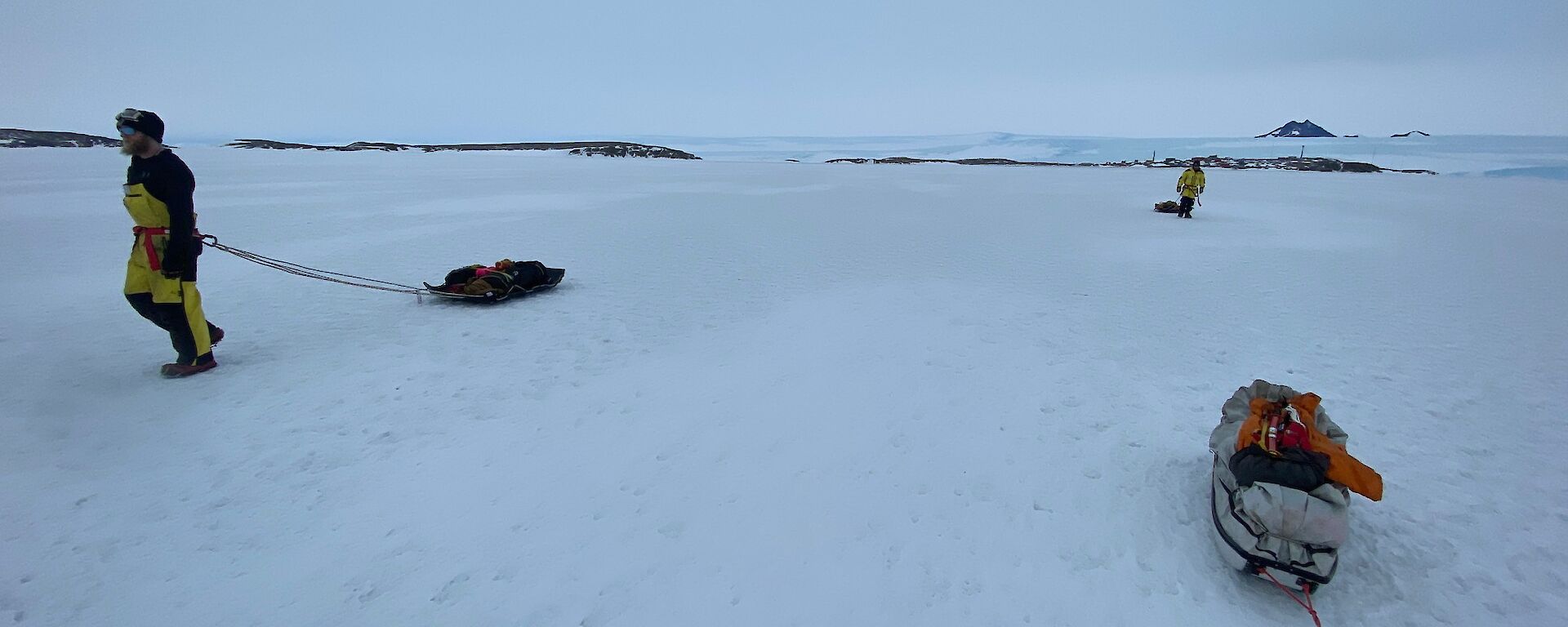 Expeditioners on the ice pulling sledges behind them attached with rope around their waists