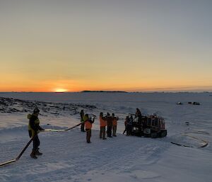A team packing up a long hose with sun setting on horizon