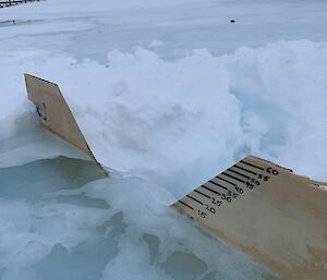 A wooden flow meter sitting in the water with measurements written on in black pen