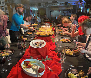 Long table with food dishes down the middle and people along each side eating