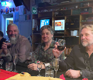 Three expeditioners smiling at the camera holding glasses of red wine