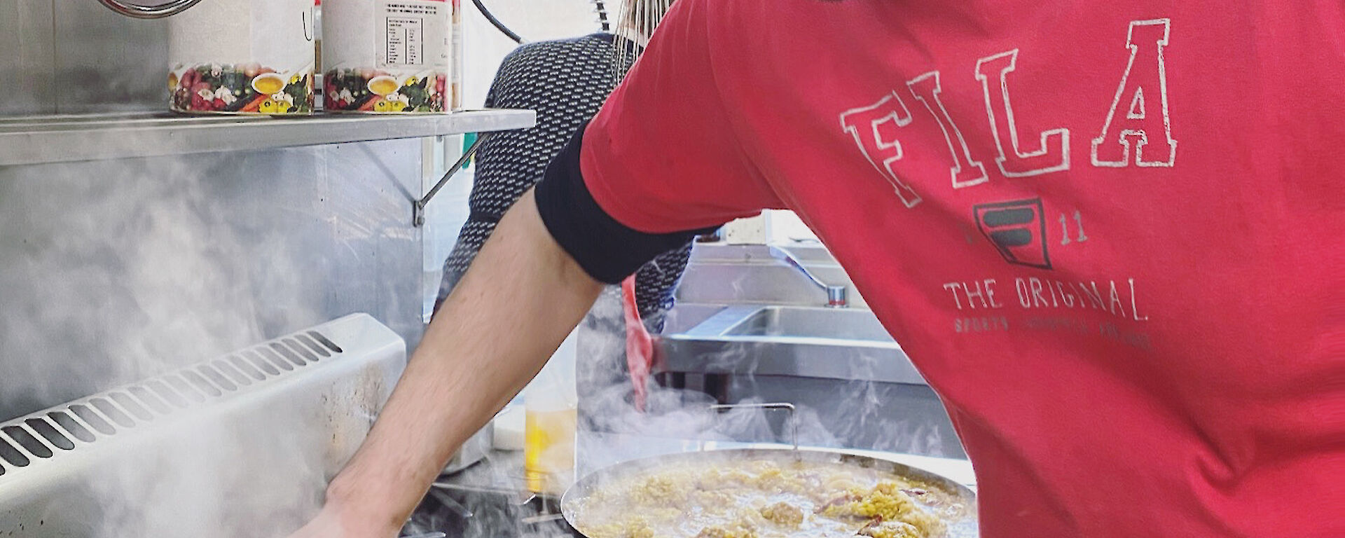 Chef standing over paella pan on stove stirring up rice