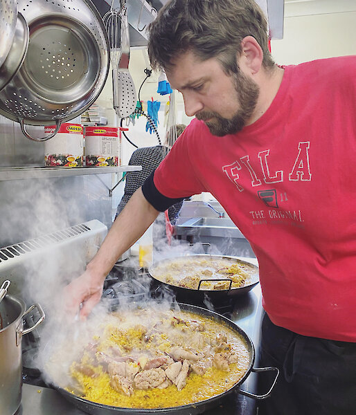 Chef standing over paella pan on stove stirring up rice