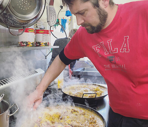 Chef standing over paella pan on stove stirring up rice