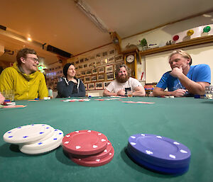 Piles of poker chips in the foreground with four people behind it playing cards