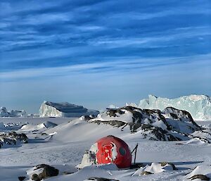 A frozen landscape with a red hut in the middle