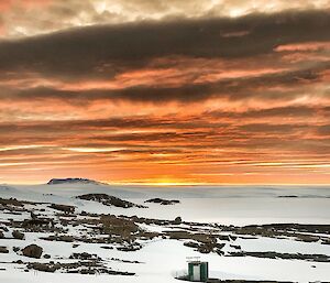 A frozen landscape against an orange sunset sky