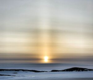 A frozen landscape with a sun pillar in the sky