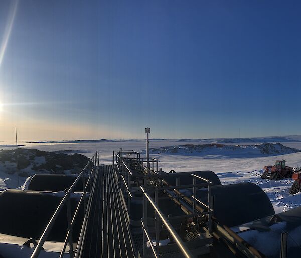 Looking out over the top of 6 fuel tanks, two tractors parked at the side, towards the horizon