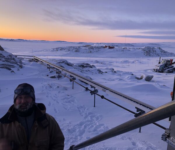 Expeditioner walking up stairs in foreground with fuel pipes behind him against a snowy landscape